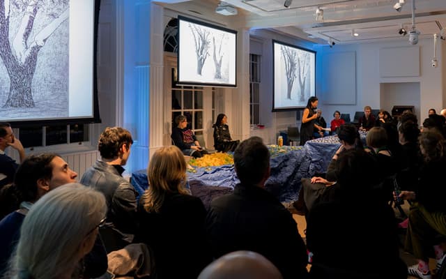 The Dream Maps event in the Lecture Hall with blue lights and people gathered around two tables with an installion of food as a landscape