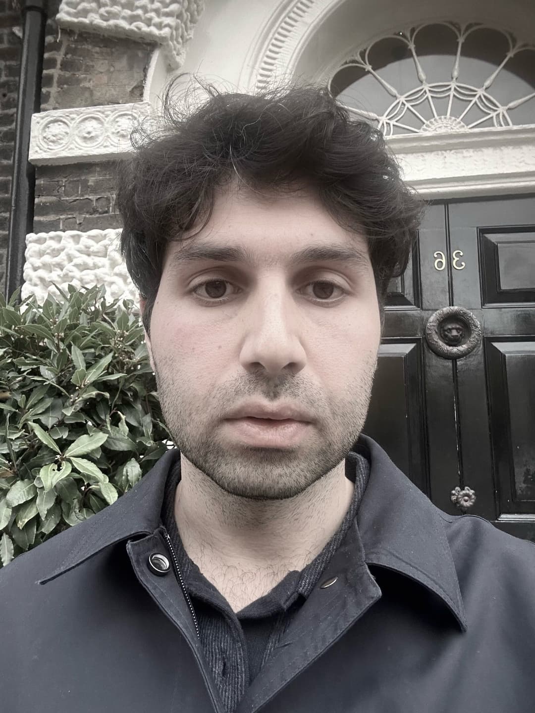 A man with dark, curly hair and a serious expression, wearing a dark collared shirt.