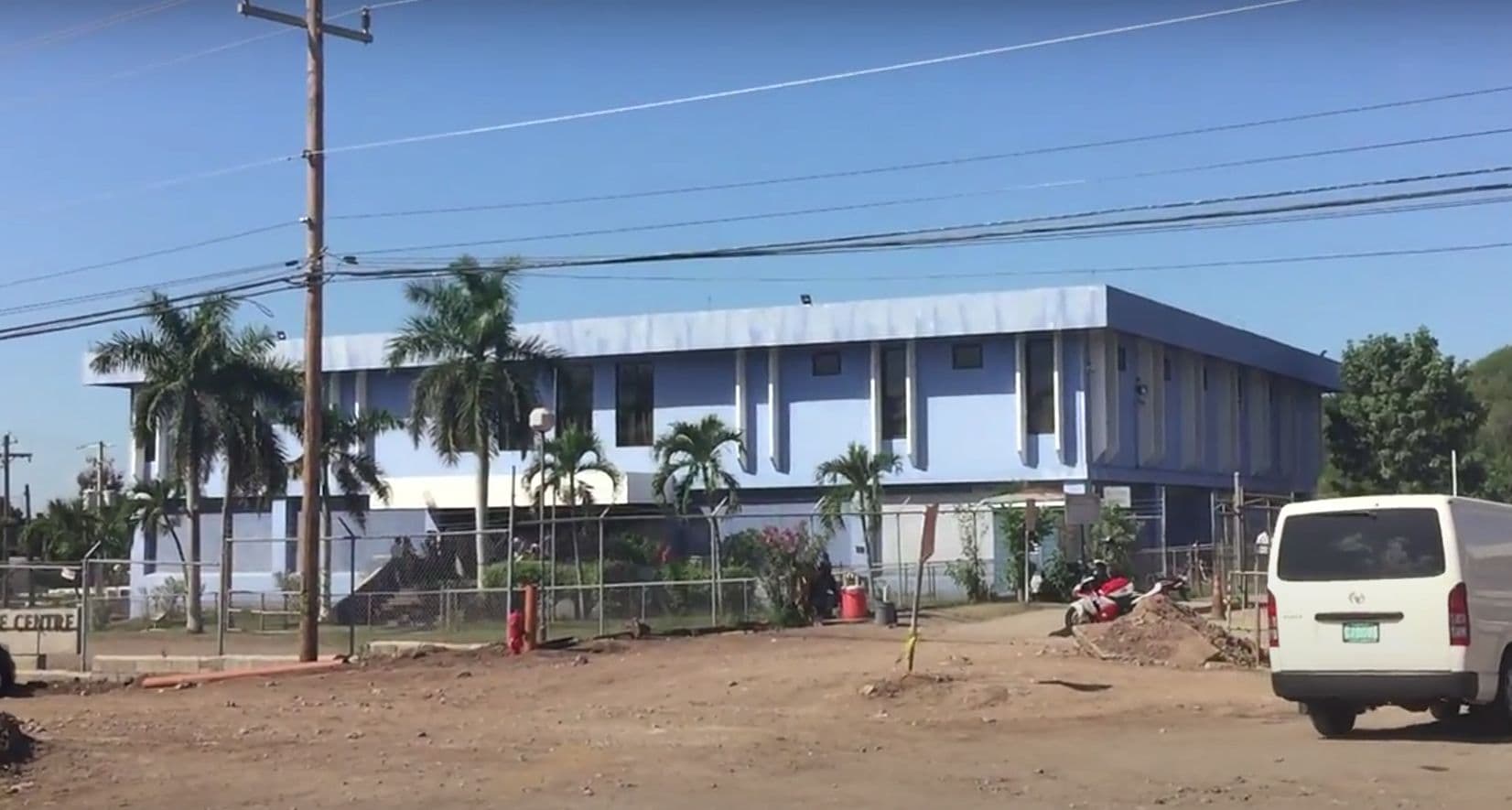 Light blue two-story building with palm trees, a fence, and a white van.