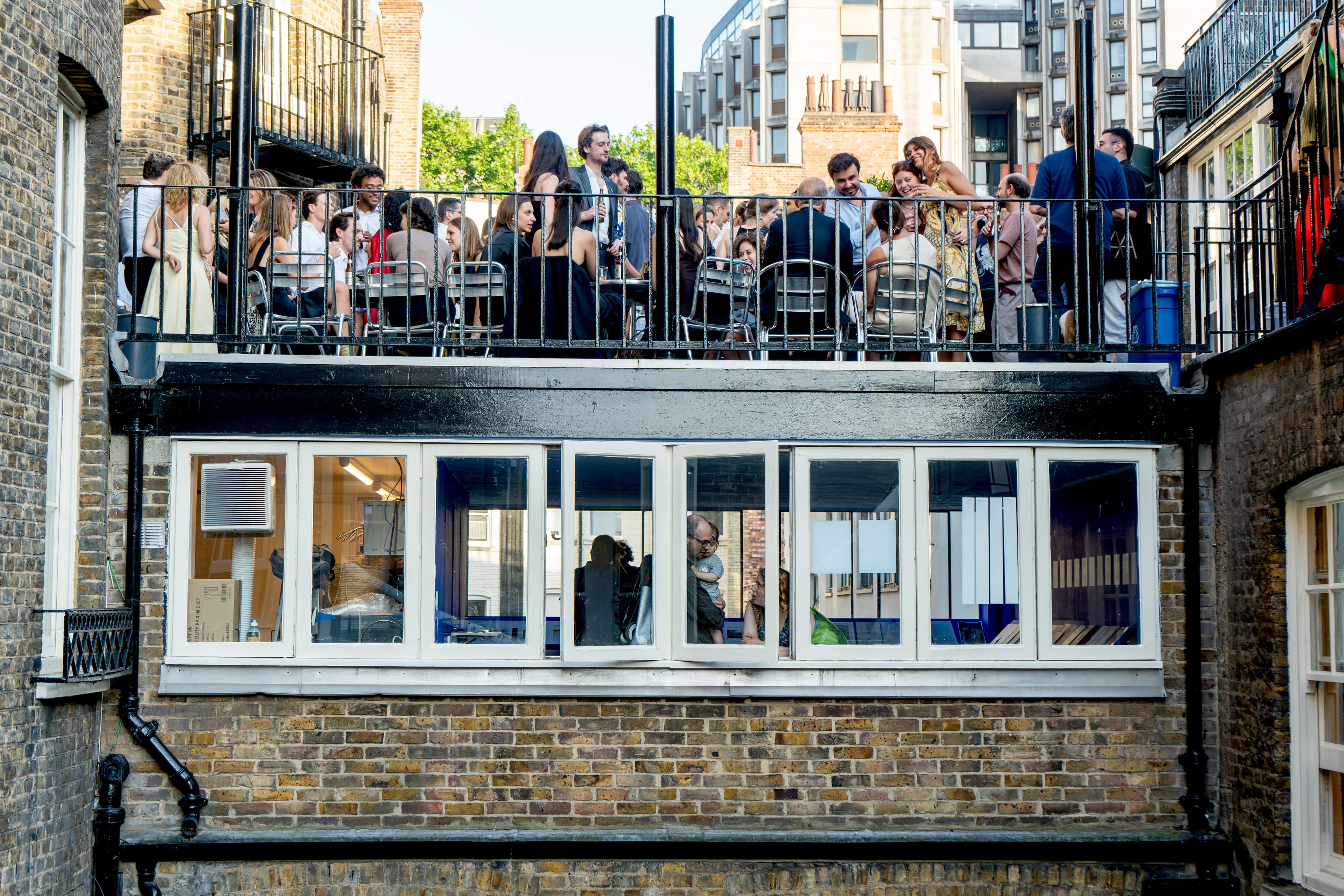 People gather on a rooftop balcony overlooking an outdoor urban space.