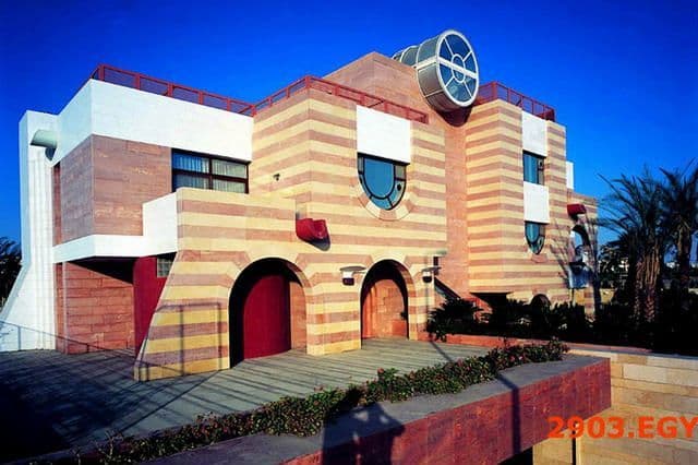Modern building with horizontal striped bricks, red accents, arched doorways, and circular windows.