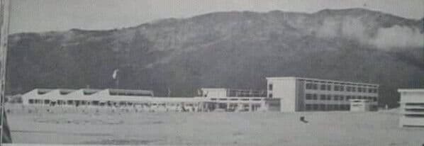 Black and white photo of campus buildings with a large, forested mountain behind them.