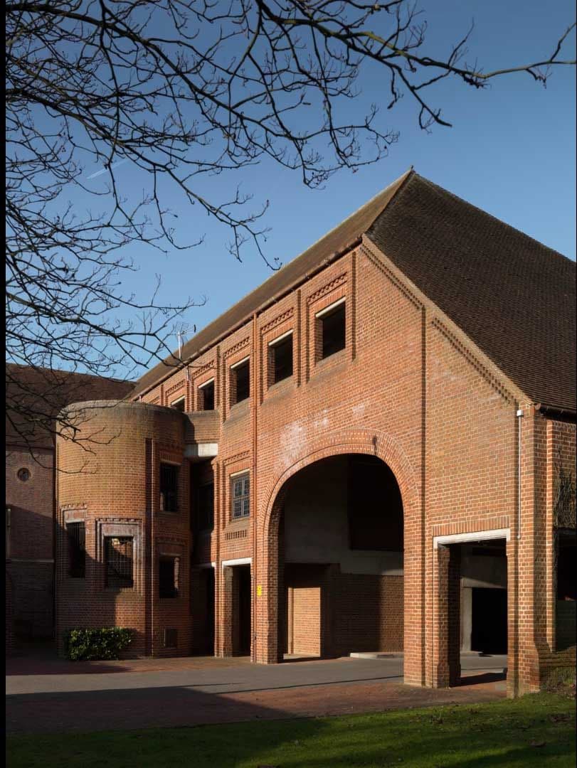 A large brick building with a prominent archway and a round tower under a blue sky.