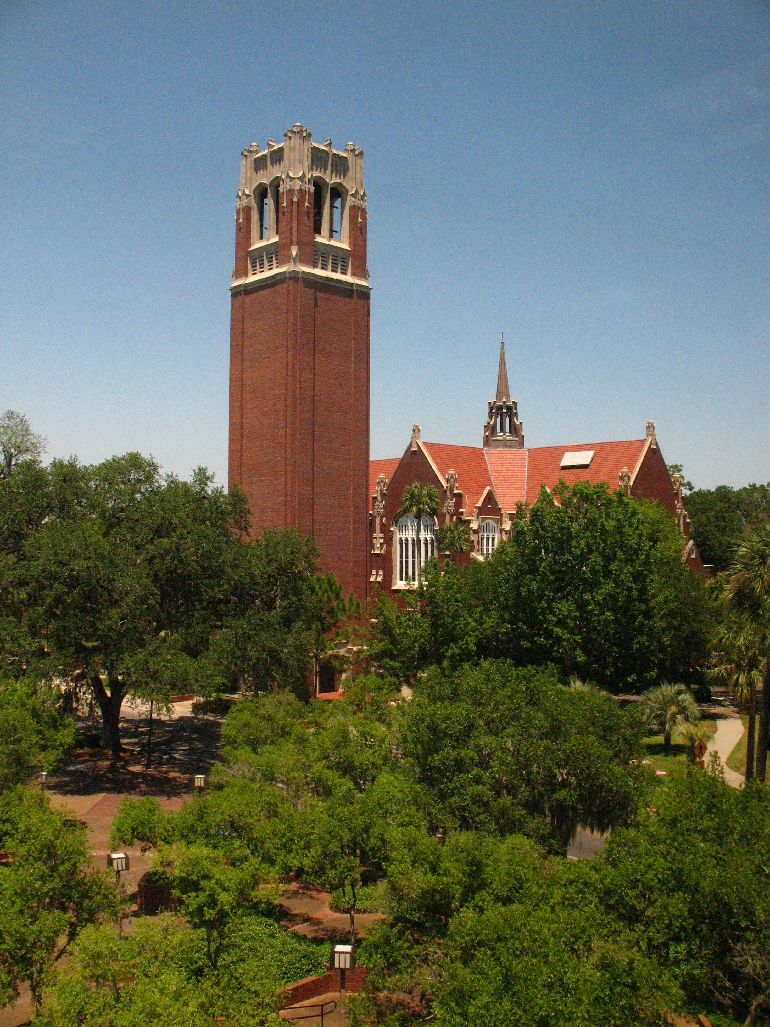 Brick clock tower with a square base and a pyramidal roof on a sunny day.