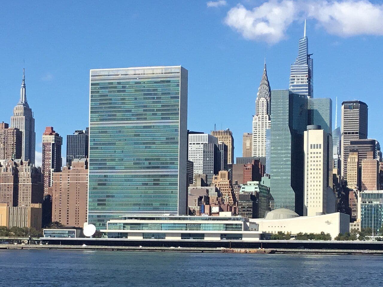 The United Nations Headquarters building stands prominently with the New York City skyline behind it.