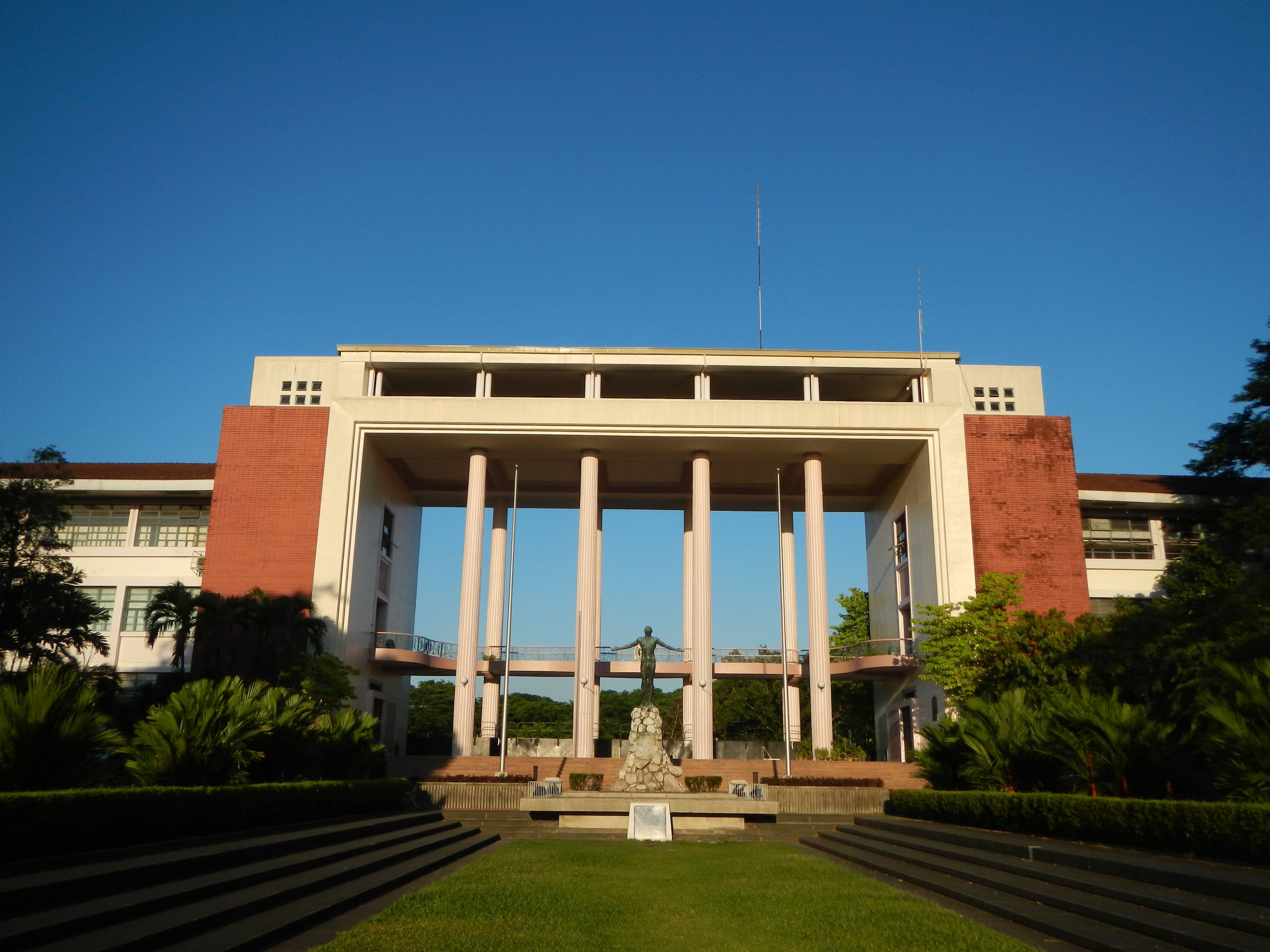 A grand, columned building with a statue and wide lawn under a clear blue sky.
