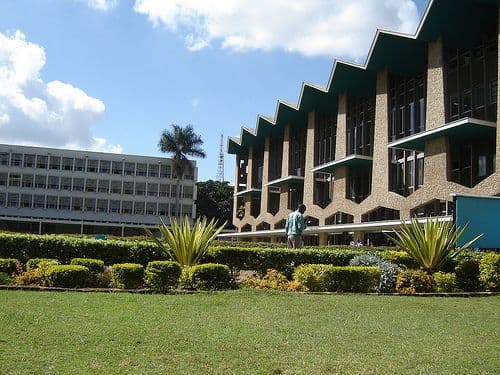 Two distinctive buildings with green lawns and shrubbery under a partly cloudy sky.