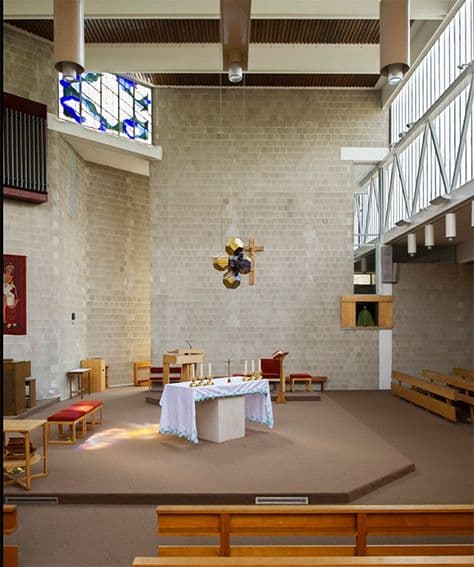 Modern church interior with altar, stone walls, and a distinctive stained-glass window.