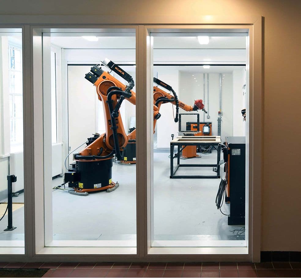 Two industrial robotic arms are visible inside a clean, white laboratory or factory room.