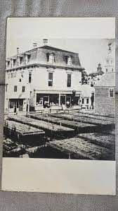 Historic multi-story building with a mansard roof overlooks a street with parked cars and storefronts.