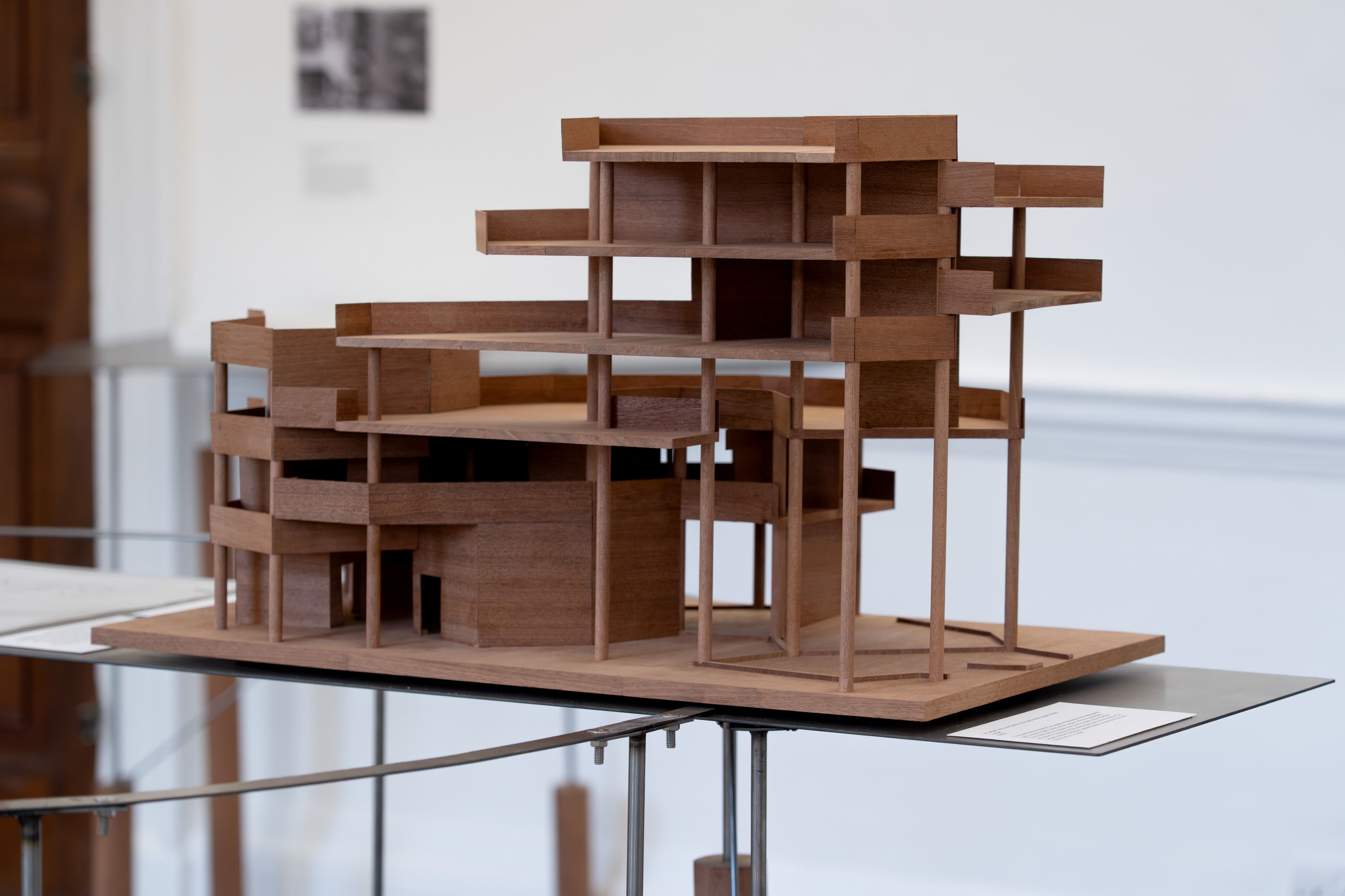 A wooden model building sits on a metal table in a white room.