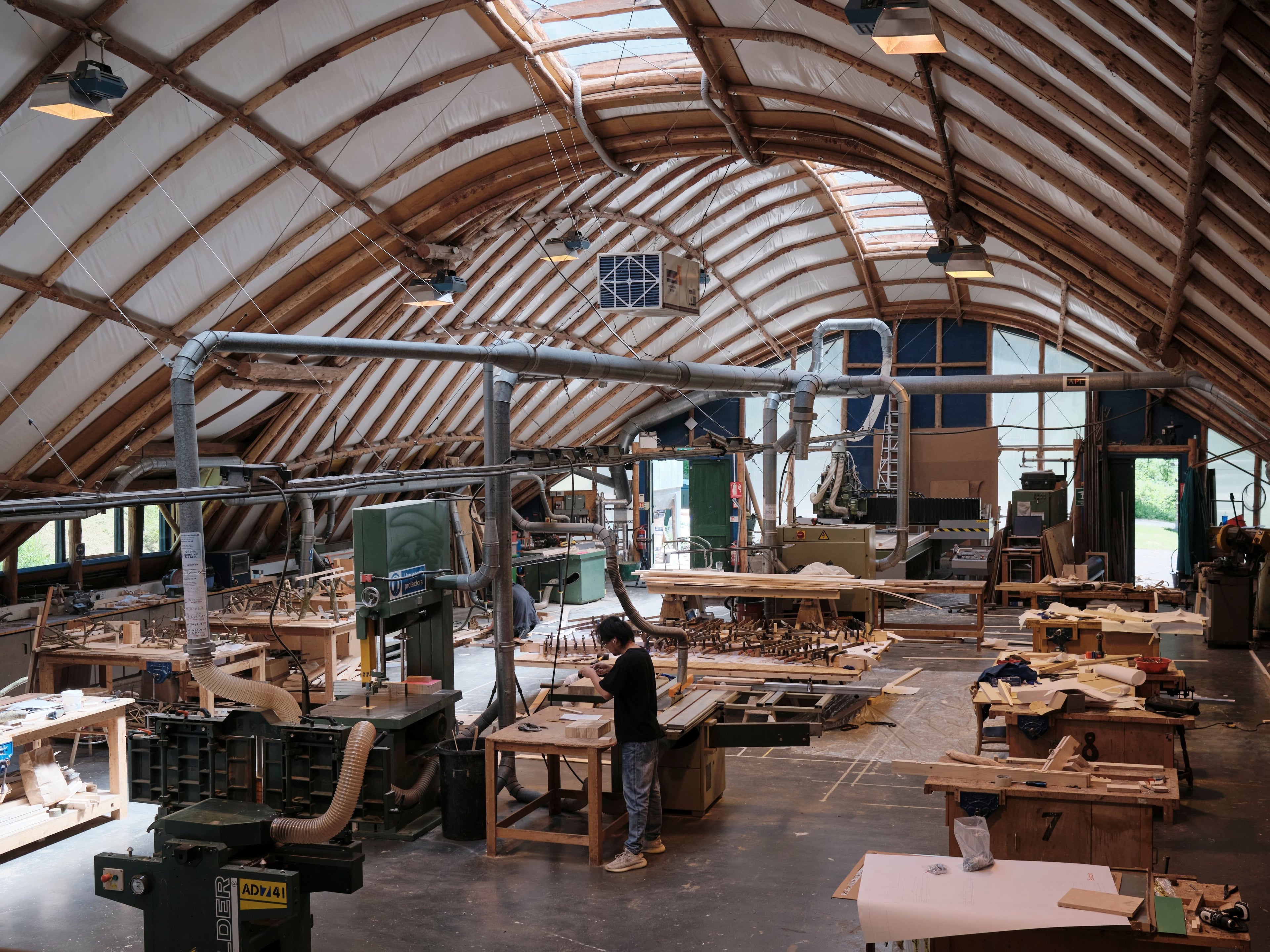 A large workshop with a curved timber roof, filled with woodworking machinery.