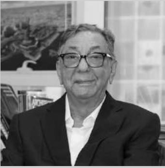 Black and white portrait of a smiling man with glasses wearing a suit.