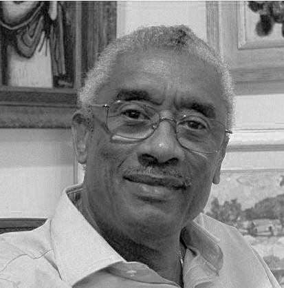 Black and white portrait of an older man with glasses, smiling softly.