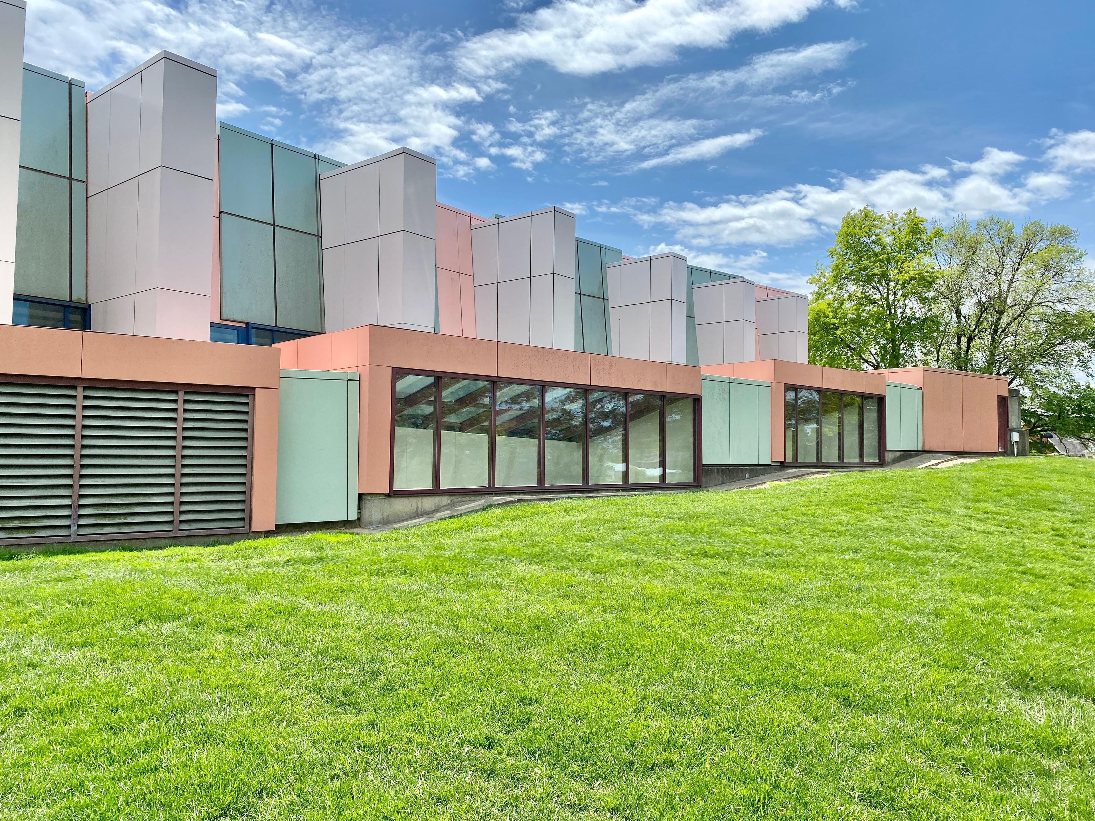 Modern building with coral and white facade, large windows, and a green lawn under a blue sky.