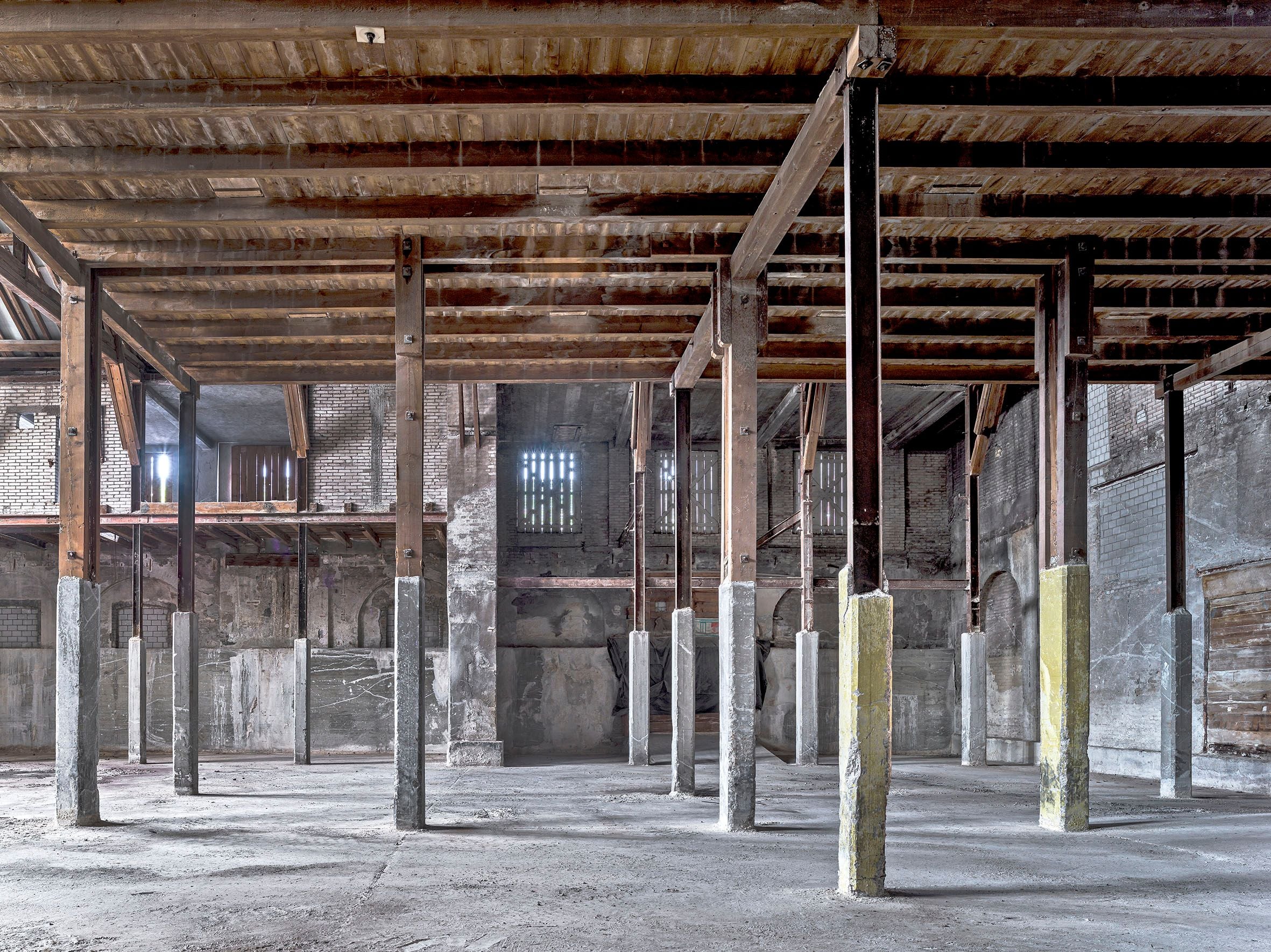 Interior of an empty warehouse with exposed wooden beams and concrete pillars.
