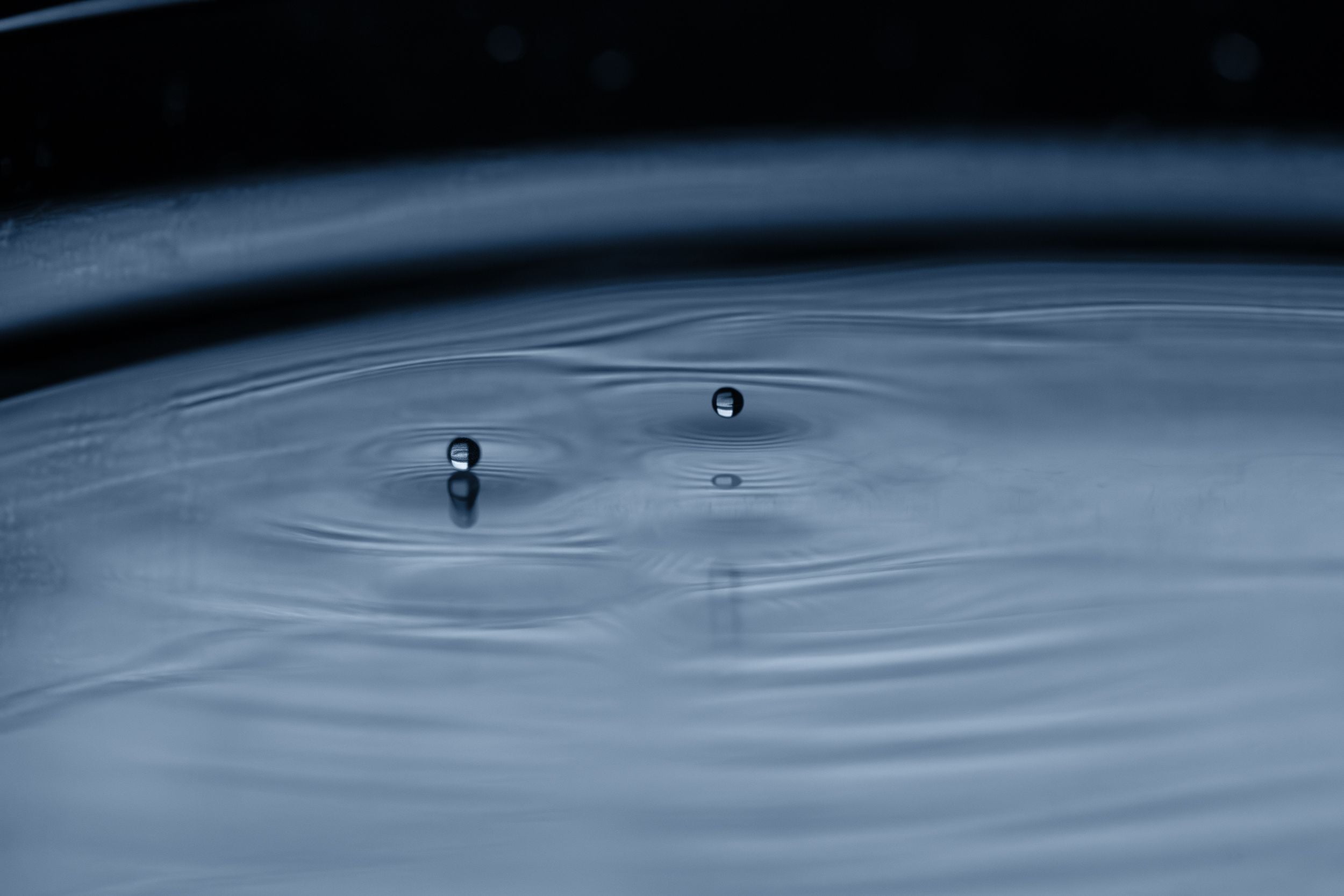 Two small water droplets suspended above rippling water's surface.