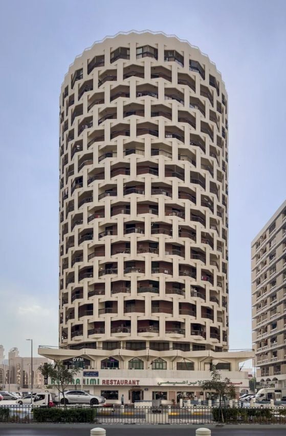 A tall, cylindrical building with many small, repeating arched windows under a clear sky.