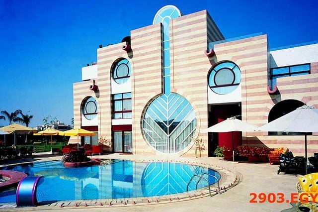 Modern building with striped facade, circular windows, and a large glass design beside a pool.