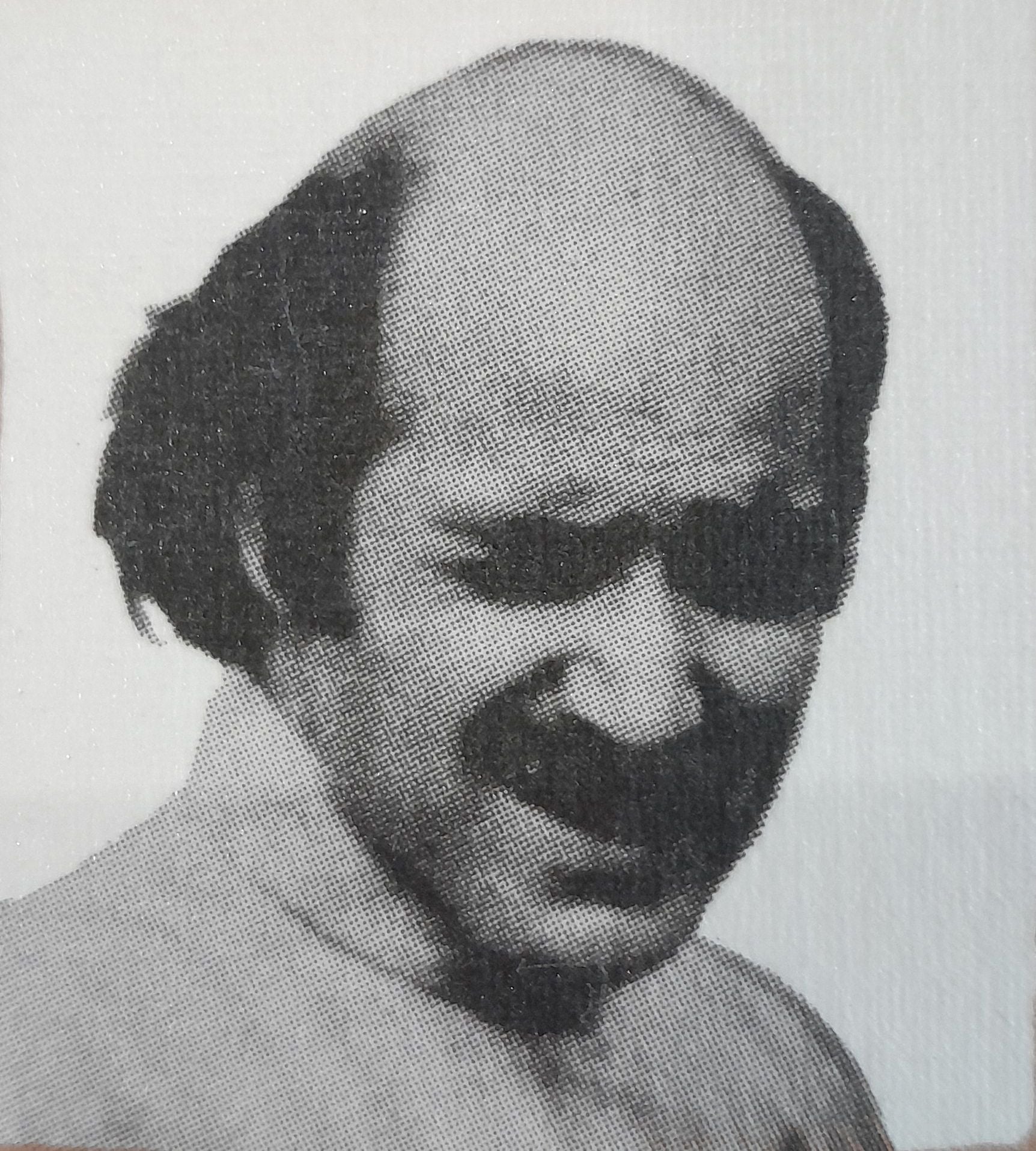 Bald man with a mustache wearing a collared shirt, looking down.
