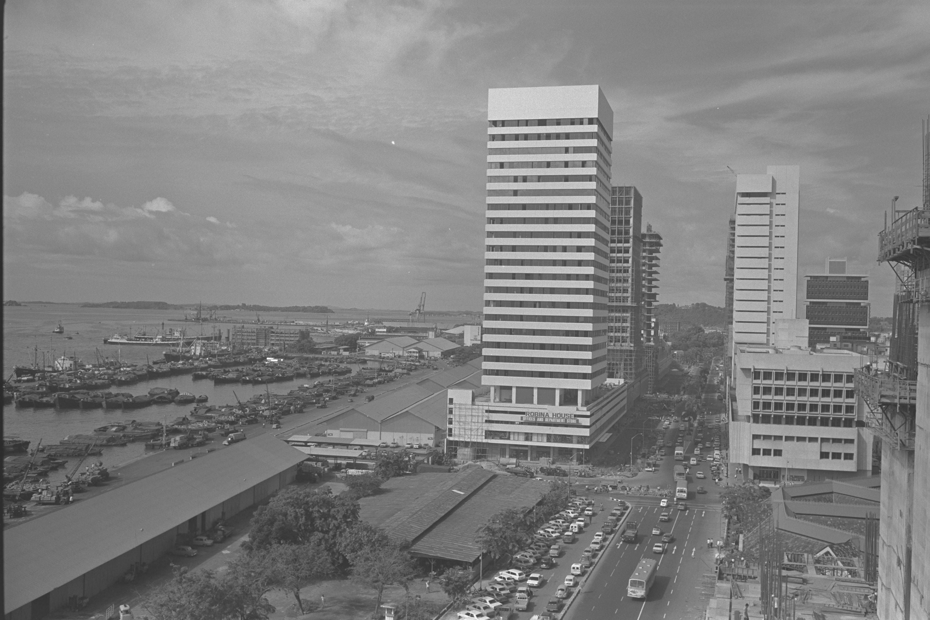A black and white aerial view of a busy port city with tall office buildings and a highway.