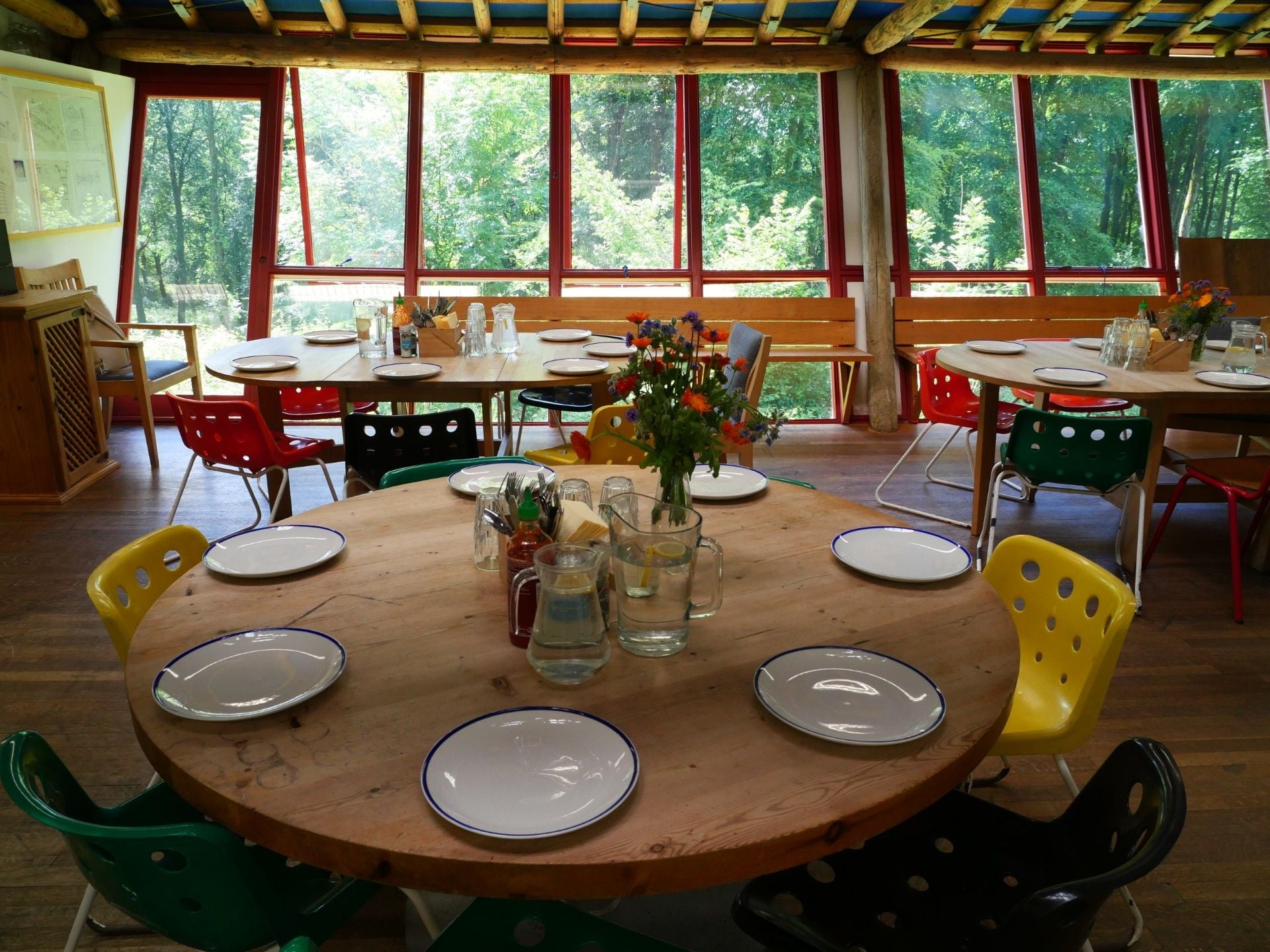 Places are set at a round dining table with yellow chairs, sitting in a timber room with windows looking out onto the woodland.