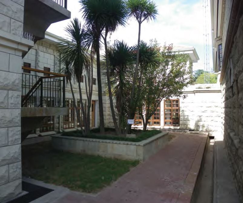 A narrow outdoor passage between stone buildings, featuring palm trees and a paved pathway.