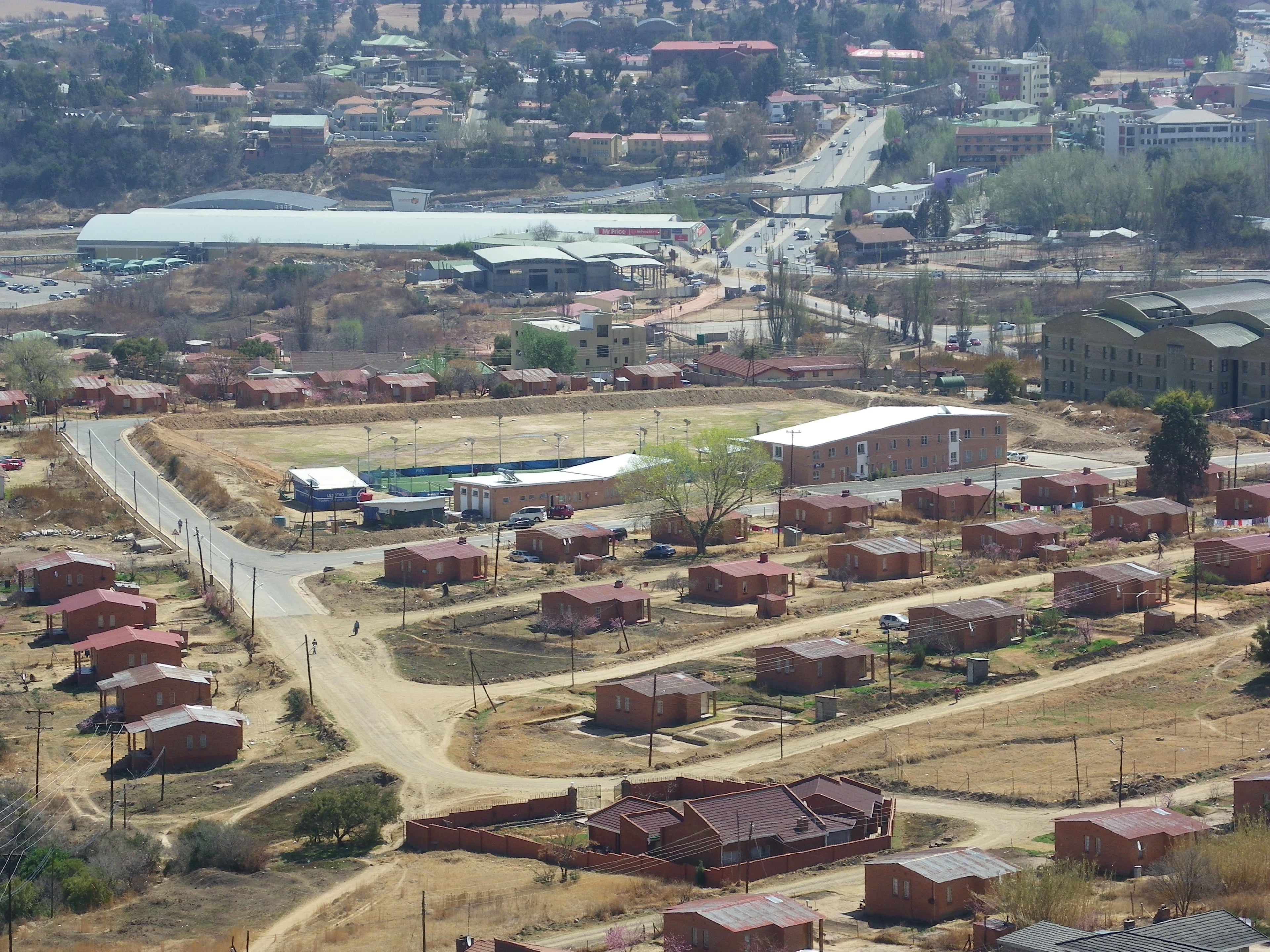 Aerial view of a town with numerous small houses, a sports stadium, and a distant highway.