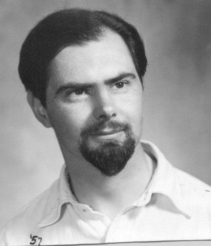 Black and white portrait of a man with a goatee, dark hair, and light shirt.