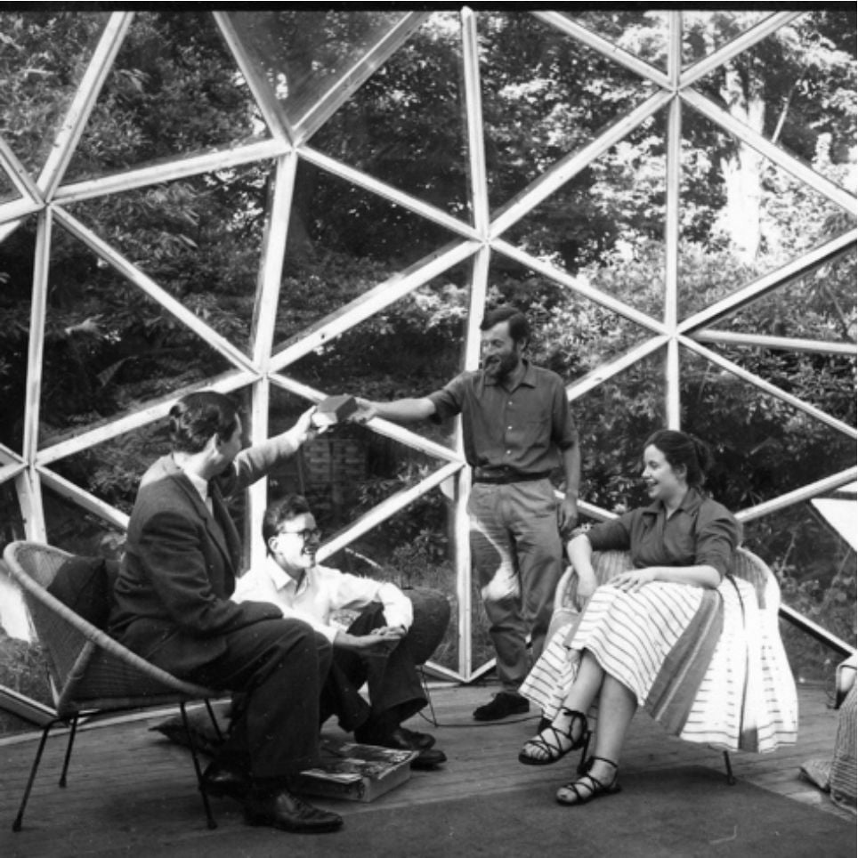 Four people conversing inside a large geodesic dome with a visible structural framework.