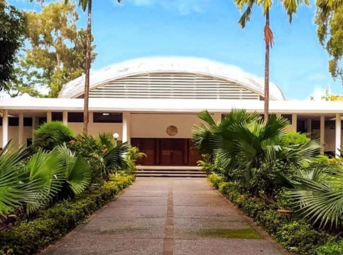 Modern building with a curved roof, pathway, and lush tropical landscaping.