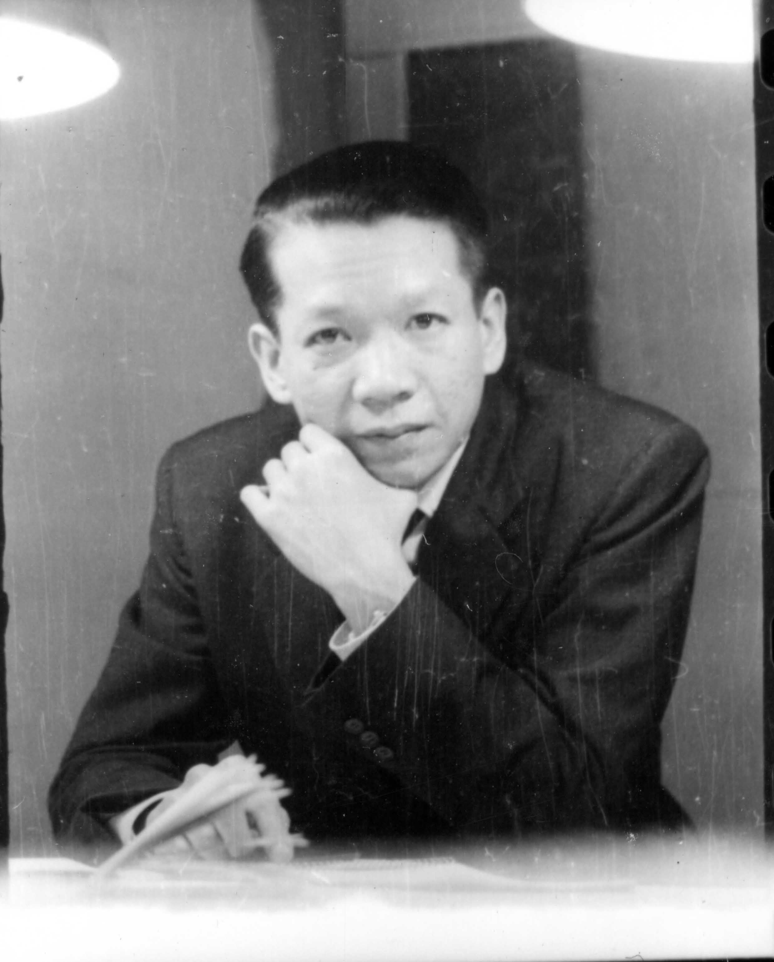 Man in a dark suit and tie, hand on chin, looking pensively at the camera.