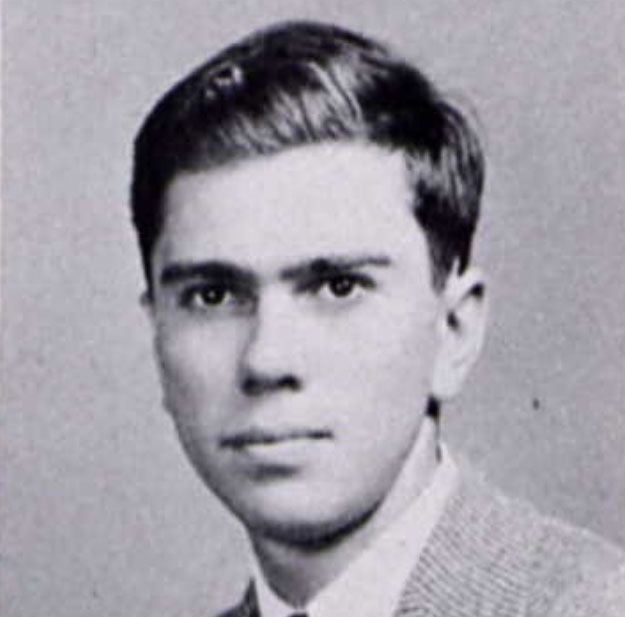 Young man with dark hair and a serious expression, wearing a collared shirt and blazer.