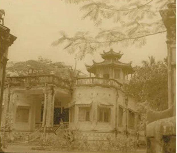 A weathered, colonial-style building with a traditional Asian pagoda-style roof sits amidst lush greenery.