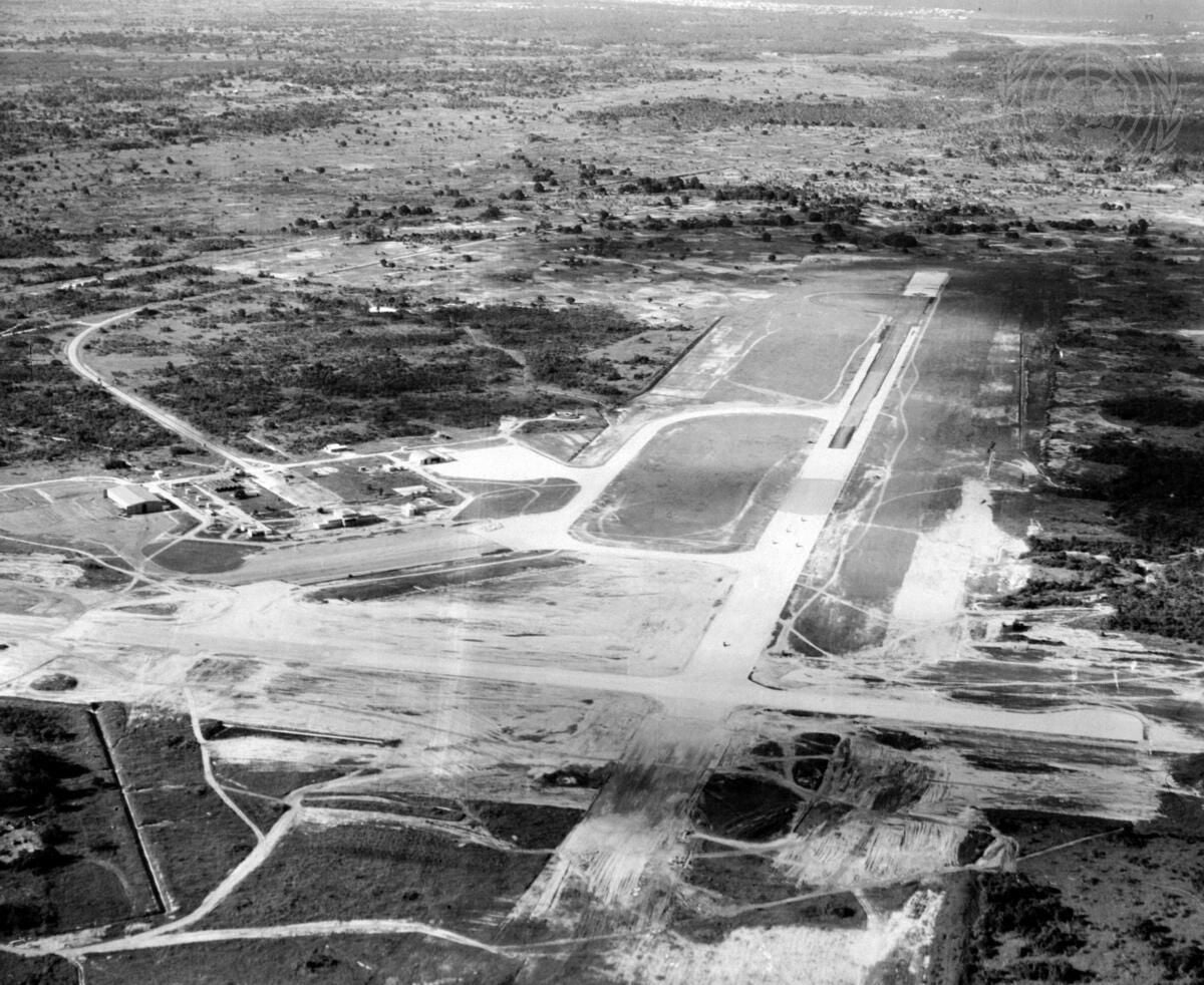Aerial view of a large airport runway with surrounding buildings and vegetation.