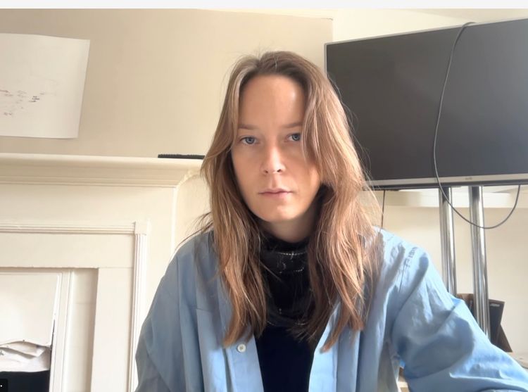 A young person with long brown hair, wearing a light blue jacket, looks forward.