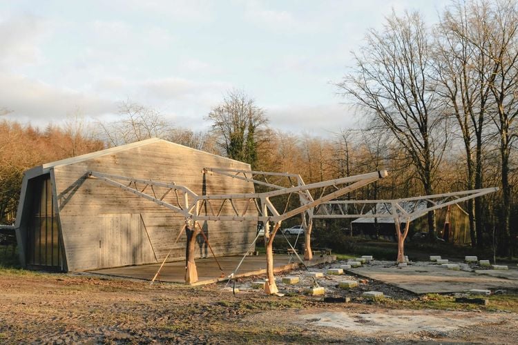 Large concrete V2 bunker with a skeletal framework in a wooded, open field.