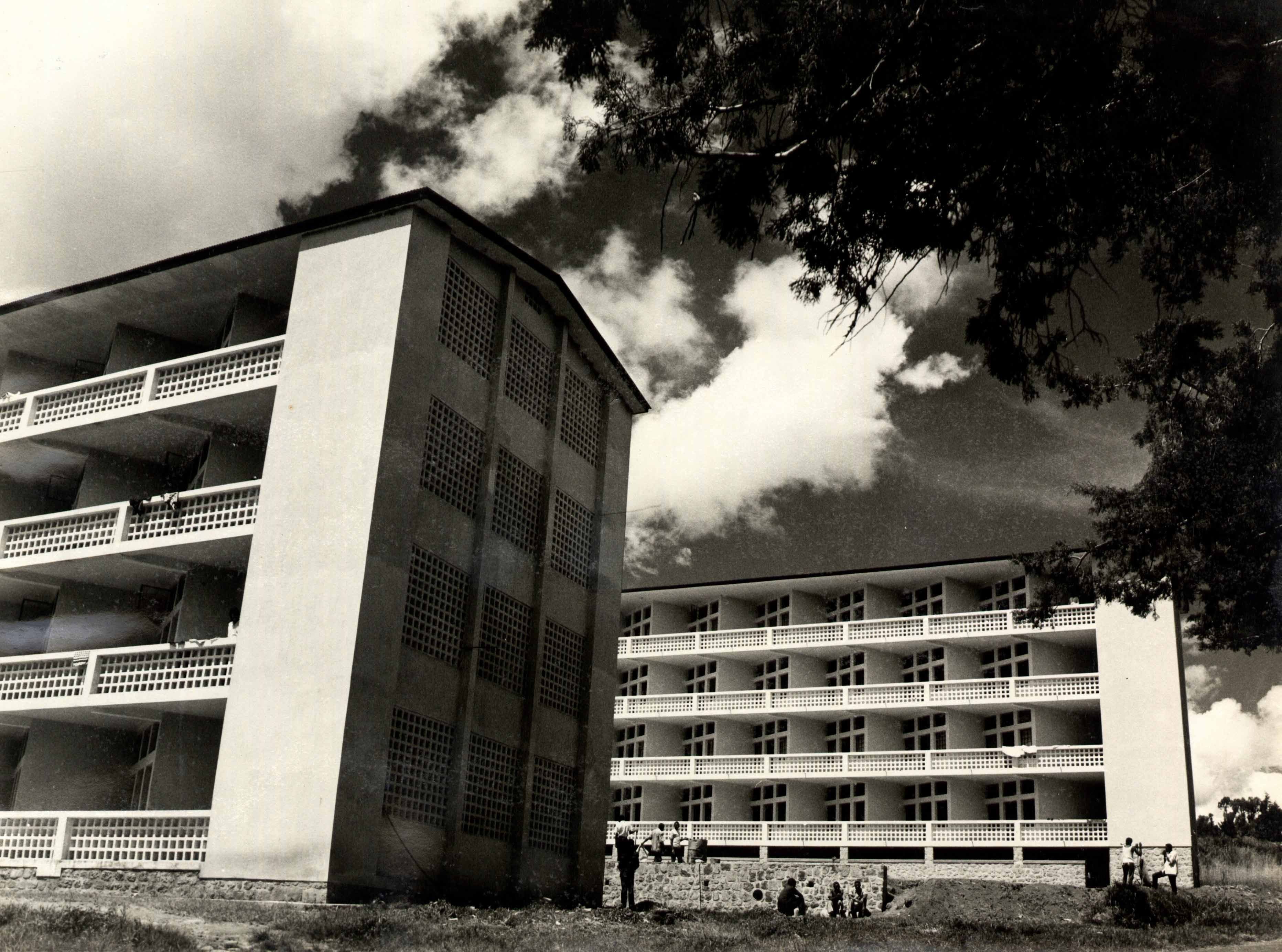 Two mid-century modernist apartment buildings with balconies stand under a dramatic cloudy sky.
