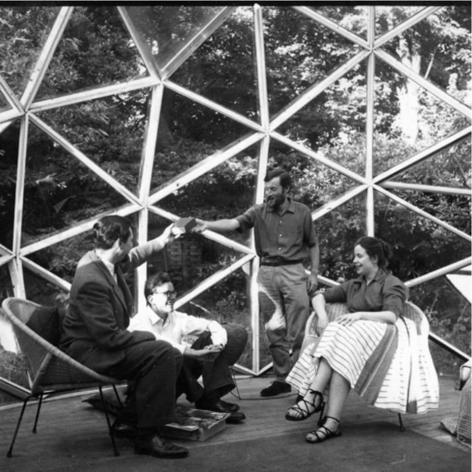 Four people conversing inside a large geodesic dome with a visible structural framework.