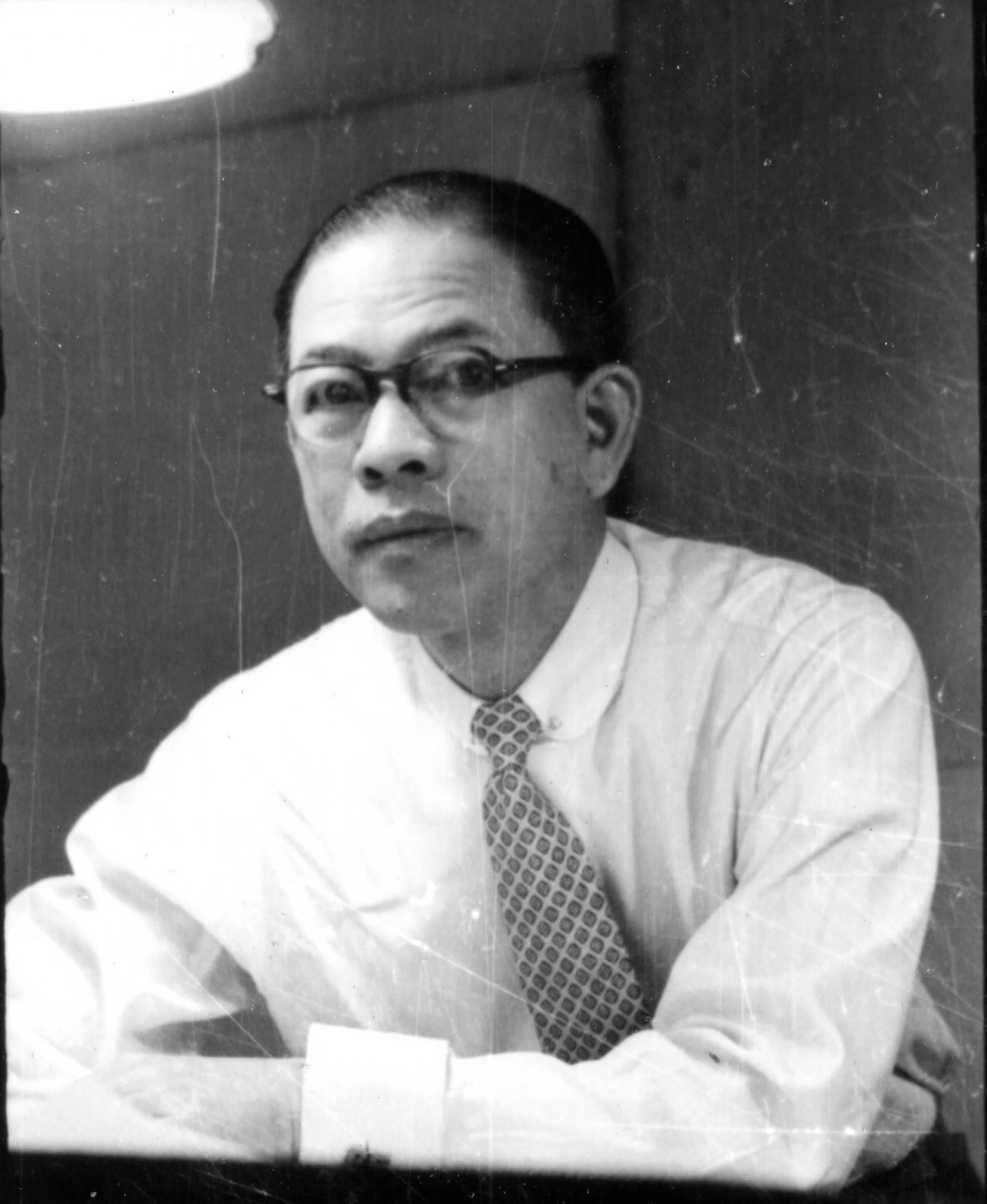 Man with glasses, white shirt, and patterned tie looking seriously at the camera.